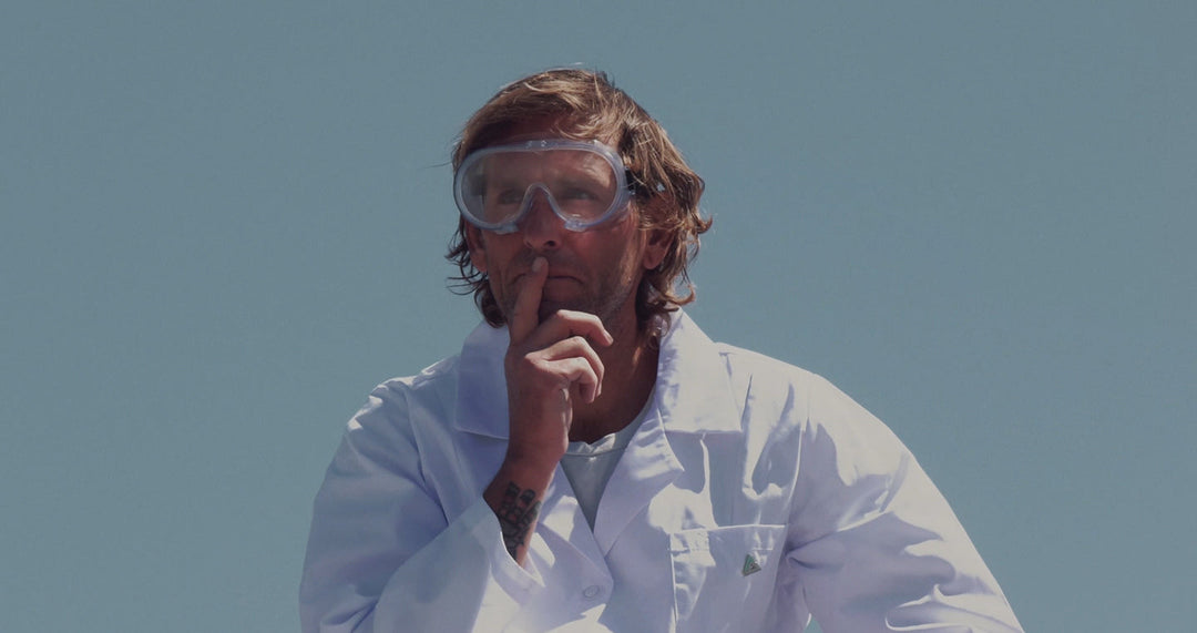 Upcycled Coconut Boardshorts. Man in scientist outfit with goggles shushing the camera